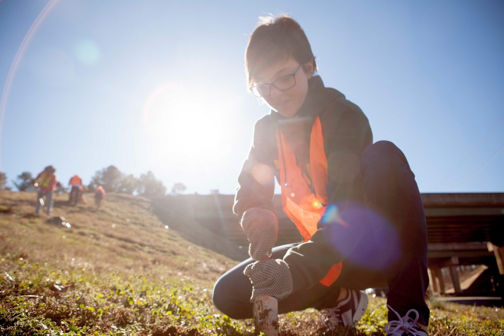 A student planting flowers on the side of a highway during the MLK day of Service.