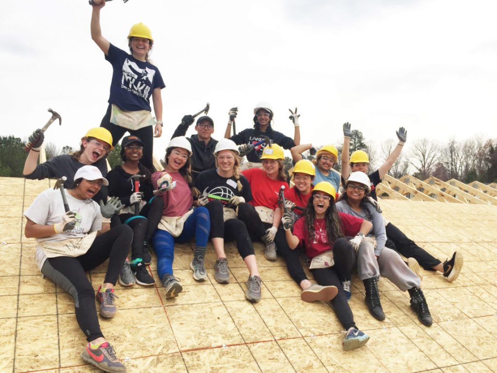 Students posing with hardhats on and are holding hammers in the air